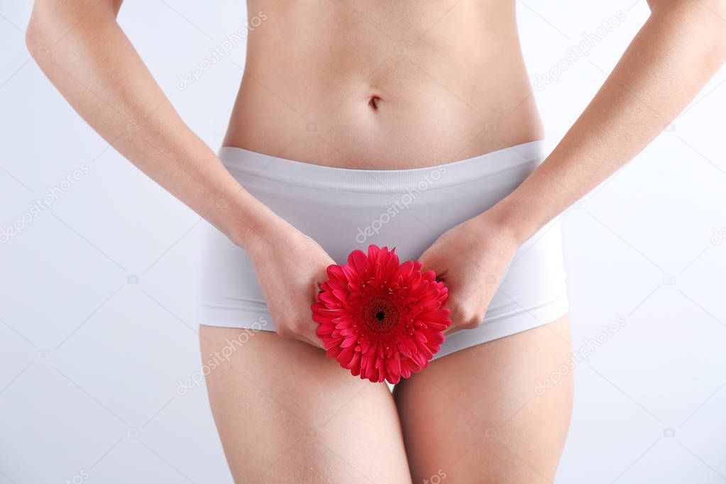 Young woman holding flower near underwear on white background. Gynecology