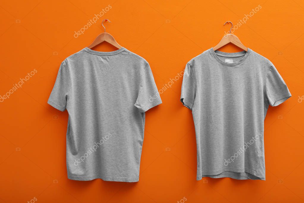Hangers with blank t-shirts on color background. Mockup for design