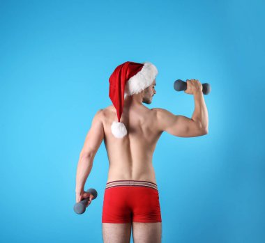 Gömleksiz seksi genç Noel Baba renk arka plan üzerinde dumbbells ile