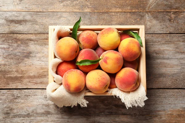 Wooden crate with fresh sweet peaches on table, top view