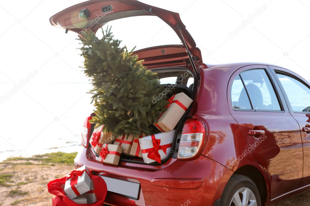 Red car with gift boxes and Christmas tree on beach. Santa Claus delivery