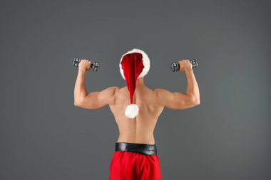 Gömleksiz seksi genç Noel Baba renk arka plan üzerinde dumbbells ile