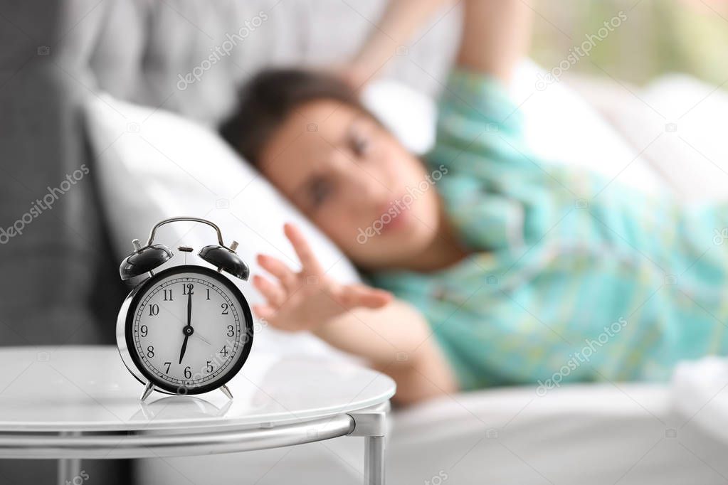 Alarm clock on table and woman in bedroom. Sleeping time