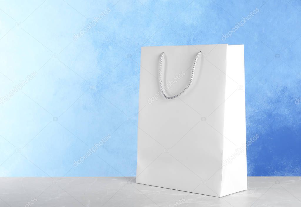 Mockup of paper shopping bag on table against color background