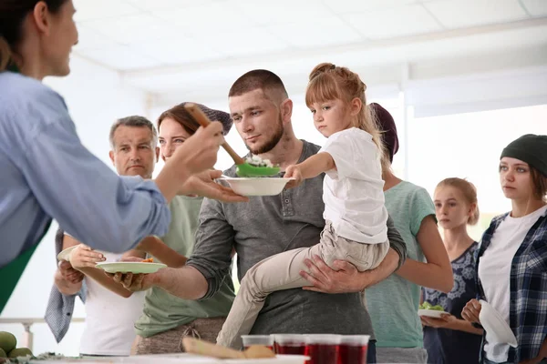 Volunteers serving food for poor people indoors