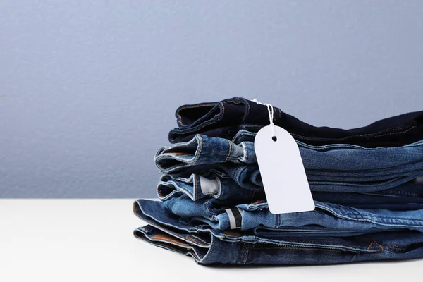 Stapel Van Stijlvolle Jeans Met Tag Tafel — Stockfoto