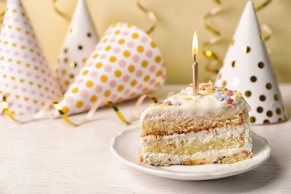 Slice of delicious birthday cake with candle on table