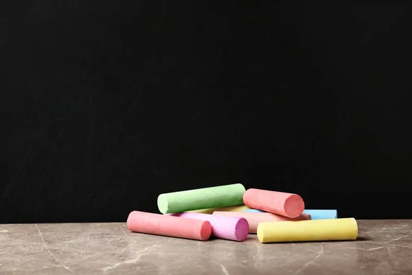 Color pieces of chalk on table near blackboard