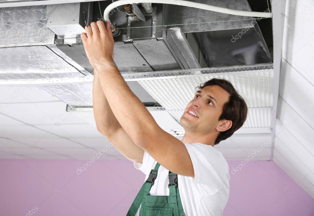 Young male technician repairing air conditioner indoors