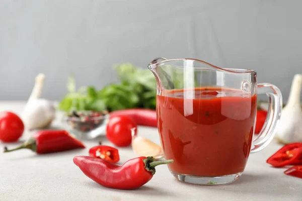 Jug with spicy chili sauce on light table