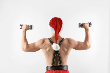 Beyaz arka plan üzerinde dumbbells ile Noel Baba şapkalı kaslı delikanlı