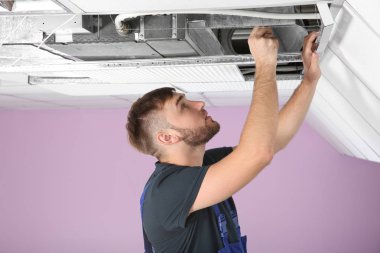 Genç erkek teknisyen içeride klima tamir ediyor.
