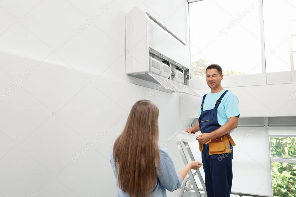 Technician speaking with woman while cleaning air conditioner indoors