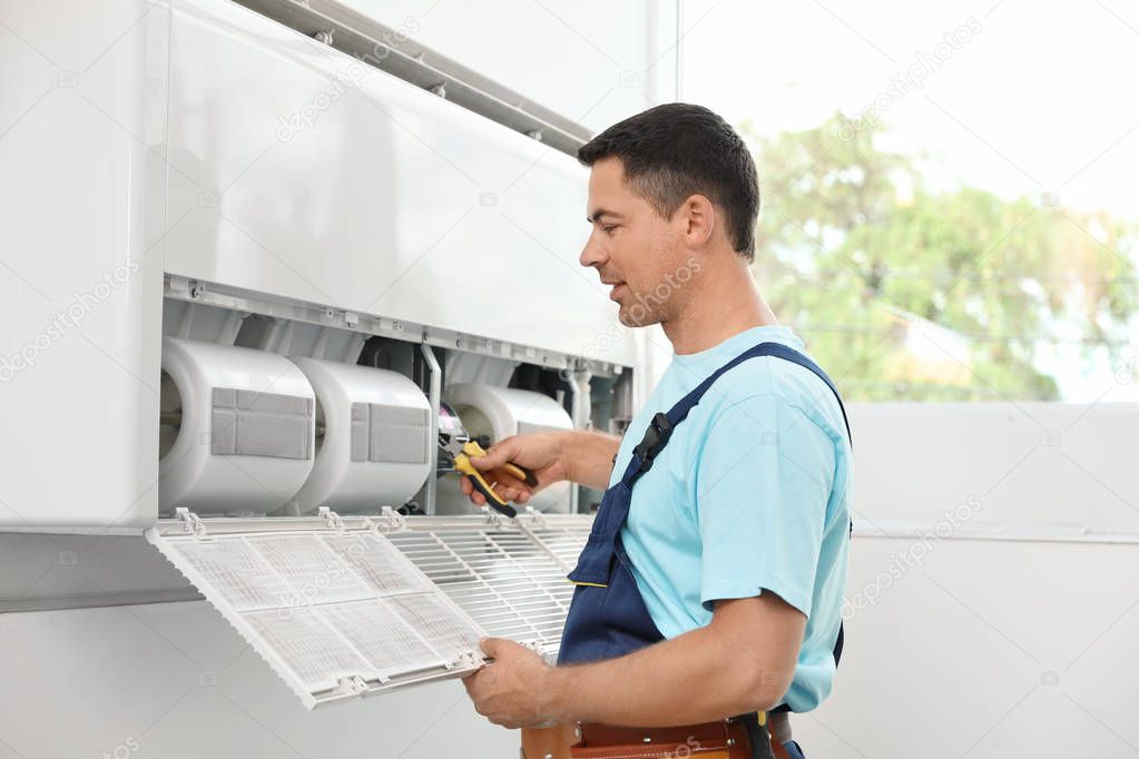 Male technician repairing modern air conditioner indoors