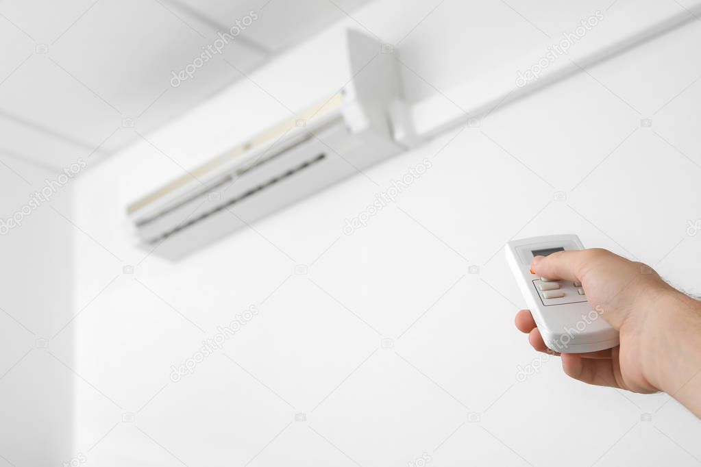 Man operating air conditioner with remote control indoors