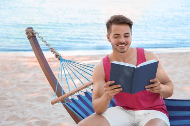 Genç adam, sahil hamakta kitap okumak