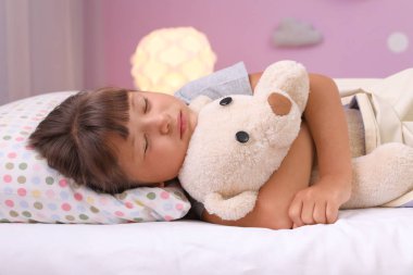 Küçük kız oyuncak ayı evde yatakta yatıyor