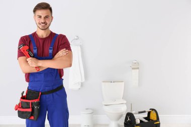 Arka plan üzerinde tesisatçı anahtarı ve tuvalet kase ile genç adam