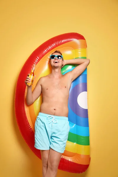 Shirtless man with inflatable mattress and bottle of drink on color background