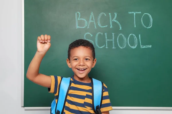 Little African-American child near chalkboard with text BACK TO SCHOOL