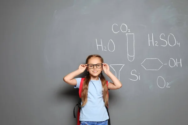 Little school child with backpack and chemical formulas on grey background