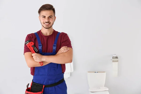 Young man with plumber wrench and toilet bowl on background