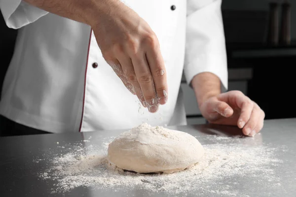 Man sprinkling dough for pastry with flour on table