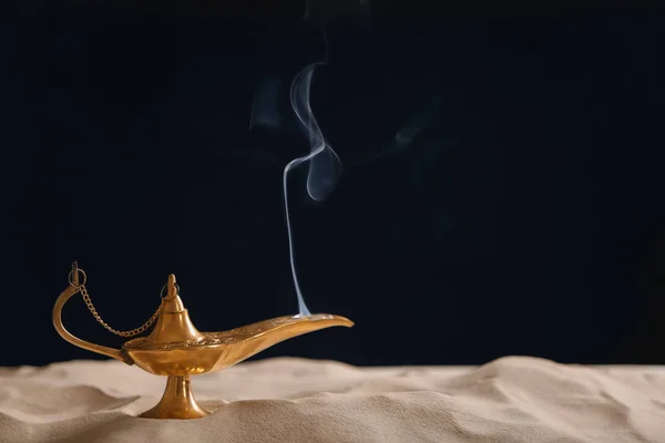 Aladdin lamp of wishes on sand against black background