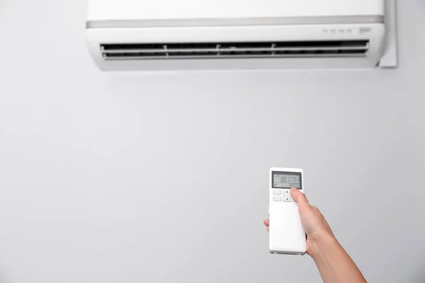 Woman operating air conditioner with remote control indoors, focus on hand