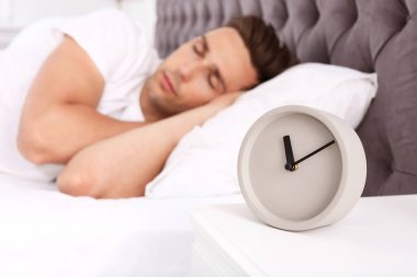 Genç adam yatakta ve çalar saat evde komodinin üzerinde uyuyor