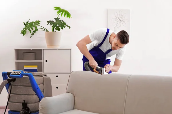 Dry cleaning worker removing dirt from sofa indoors