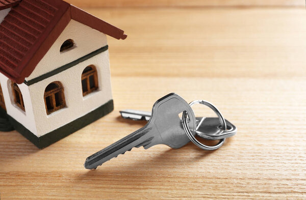 Keys and house model on wooden table. Real estate agent services