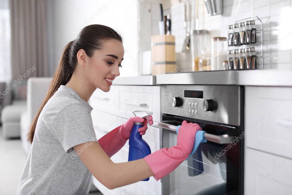 Young woman cleaning oven with rag in kitchen