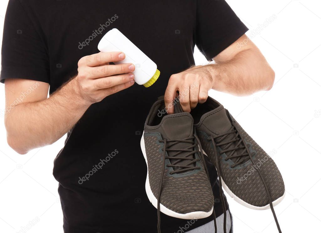 Young man putting powder freshener into shoes on white background