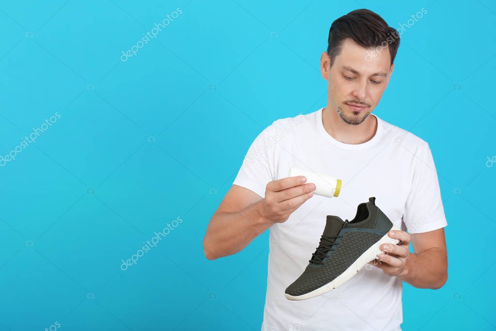 Man putting powder freshener into shoe on color background