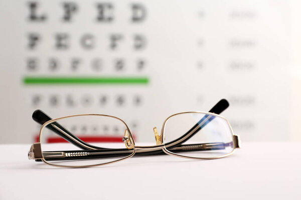 Glasses with corrective lenses on table against eye chart