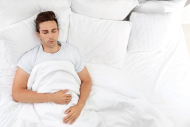 Genç adam yatakta evde yumuşak yastık uyku