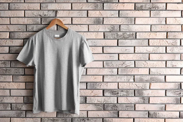 Hanger with blank t-shirt on brick wall. Mockup for design