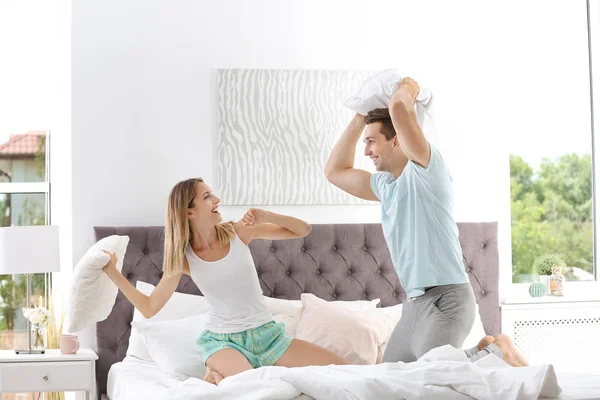 年轻夫妇在床上枕头打架在家 — 图库照片