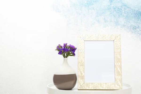 空白のフレームと光の壁の近くのテーブルの上に花と花瓶 デザインのために模擬します — ストック写真