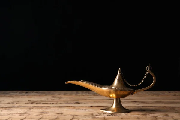 Aladdin lamp of wishes on wooden table against black background