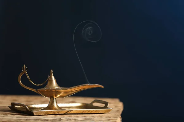 Aladdin lamp of wishes on wooden table against dark background