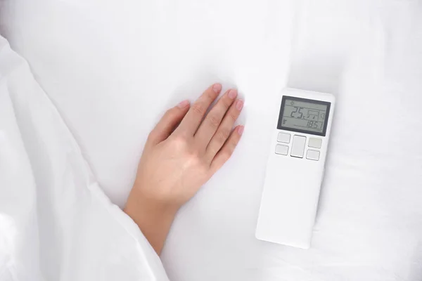 Woman with air conditioner remote control in bed, focus on hand