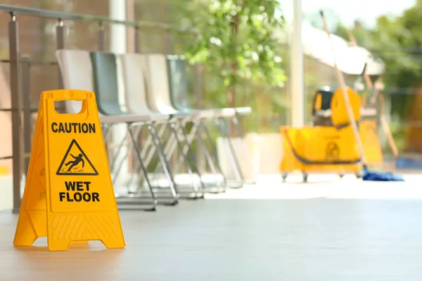 Safety sign with phrase Caution wet floor and blurred mop bucket on background. Cleaning service