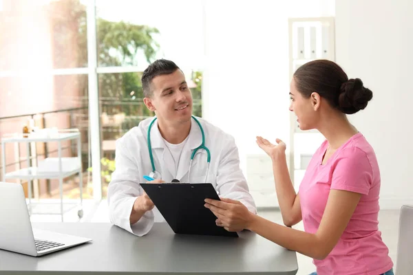 Young doctor listening to patient's complaints in hospital