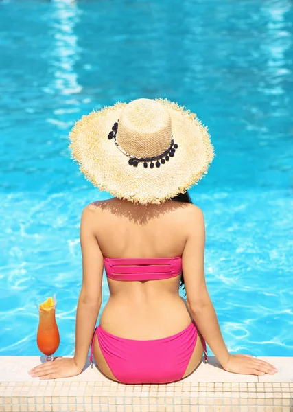 Young woman with cocktail sitting near swimming pool