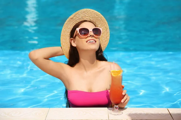 Beautiful young woman with cocktail in blue swimming pool