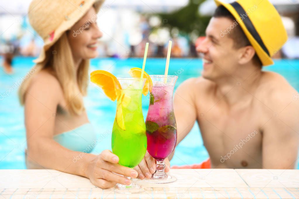 Happy couple with cocktails resting in blue swimming pool outdoors