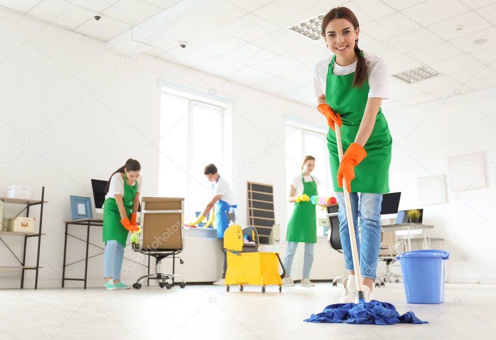 Team of professional janitors in uniform cleaning office
