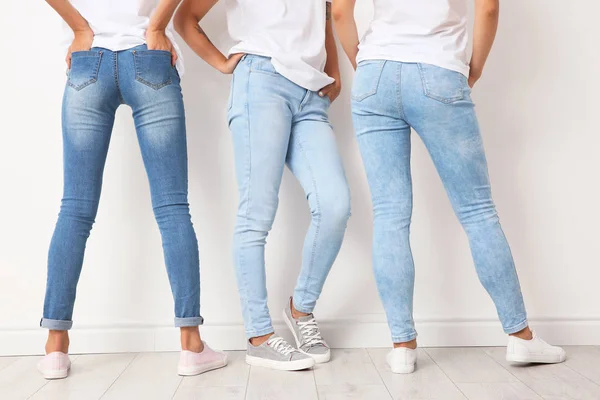 Group of young women in jeans near light wall